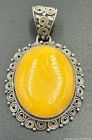 Front view showing amber cabochon and ornate silver scroll border