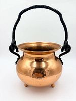 Front view of hammered copper cauldron showing body, handle, feet