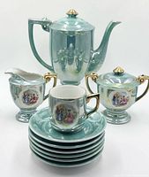 Front view showing coffee pot, creamer, sugar bowl, stack of saucers and cup displaying imagery and glaze
