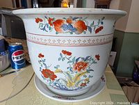 Front view of porcelain jardiniere on saucer showing floral decoration and scale reference