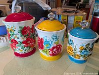 Front view of all three floral stoneware canisters with coloured lids and bases