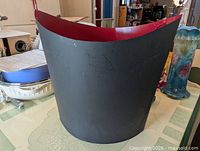 Front view of conical metal waste basket showing grey exterior and red interior