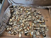 Pile of assorted souvenir spoons showing variety of handles and enamel crests