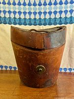 Front view of oval leather hat box showing brass lock plate and overall wear