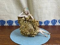 Frontal view of bisque pin cushion doll seated on fabric base