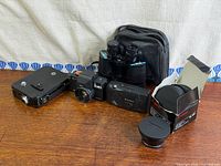 Group shot of all cameras, lens, binoculars, and case on tabletop