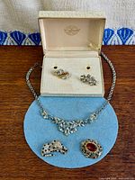 All jewellery pieces displayed: necklace, two brooches, earrings pairs in box