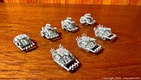 Seven metal Epic tanks grouped on wooden surface