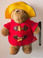 Front view of brown plush Paddington Bear in red coat and yellow hat with Sharpie for scale