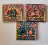 Front view of three sealed Diskwars Waiqar’s Path expansion decks showing titles and artwork