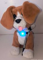 Front view of brown and white FurReal Chatty Charlie plush dog with blue lit collar and marker for scale