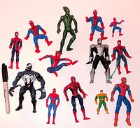 Group shot of thirteen Marvel action figures including Spider-Man variants, Venom, Green Goblin, and other villain against white background with marker for scale