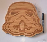 Front view of sealed bamboo Stormtrooper helmet cutting board beside marker for scale