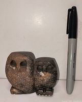 Front view of both carved stone owl figurines beside marker for scale