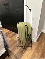 Front view of black metal folding towel/blanket stand with green throw displayed