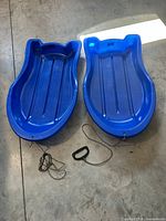 pair of blue plastic toboggans, front view showing handles and tow ropes