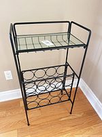 Full view of freestanding black metal wine rack showing glass top and bottle holders