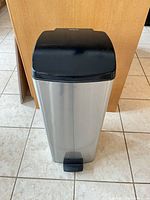 Front view of stainless steel pedal trash can with black lid and foot pedal