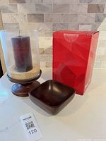 Hurricane candle holder on wooden pedestal with burgundy candle and beige sand filler beside wooden bowl and red Levoit box