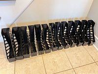 Row of 13 black plastic magazine holders on floor