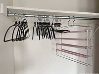 Closet rod showing black slim hangers and metal four-tier pants rack with pink straps