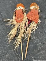 Two scarecrow yard stakes full length showing straw and wooden stakes
