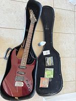 Guitar in open case with cable, strap, cleaning solution, strings visible