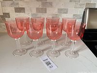 Full set of eight pink acrylic wine glasses arranged on countertop