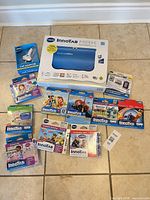 Group shot of tablet box, car adapter, 10 software cartridges, download card and manual