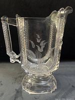 Front view of pressed glass pitcher showing etched bird and floral motif and pedestal base