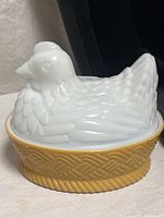 Front view of white milk glass hen lid on amber basketweave base