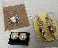 group shot showing all items: cameo necklace, faux pearl earrings, packaged hair clips