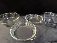 four clear glass Pyrex pieces grouped: round casserole, two round shallow dishes, rectangular loaf pan