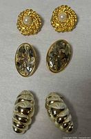 All three pairs of earrings laid out: round faux pearl, oval enamel, ribbed hoops