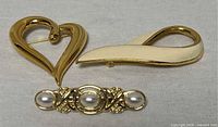All three gold tone earrings: open heart, cream enamel ribbon, faux pearl bar