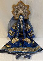 Full view of porcelain doll seated showing complete costume and headdress
