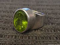 Front angled view of sterling silver ring with oval green gemstone