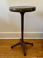 Full view of industrial metal stool showing round seat, pedestal column, four-leg base