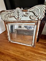 Full view of mirror showing ornate crest, distressed frame, mirror plate
