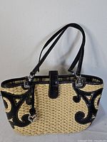 Front view of woven straw handbag with black leather scroll trim and heart charm