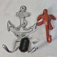 Front view of aluminum anchor hook with tag and screws beside cast-iron turtle hook