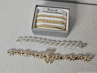 All five bracelets displayed: boxed Rembrandt trio, silver-tone rhinestone bracelet, gold-tone teddy bear bracelet