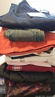 Stack of folded clothing: black top, denim jeans, rust corduroy, assorted shirts