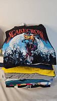 Stack of T-shirts showing top Scarecrow graphic and colours of other shirts