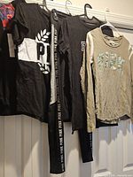 Overview of four PINK garments on hangers: two black tees, beige long-sleeve shirt, black leggings