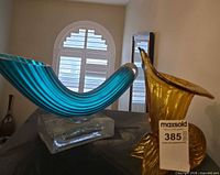 Blue curved art glass sculpture and amber vase on black surface