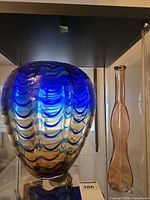 Blue patterned art glass vase beside pink bud vase in display cabinet