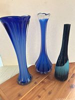 Group shot of all three blue glass vases on wood surface