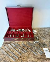 Open wood chest showing flatware pieces and additional utensils laid on countertop
