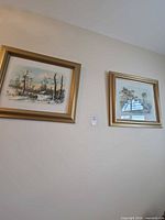 Both framed artworks on wall, subject piece is left winter scene in gold frame